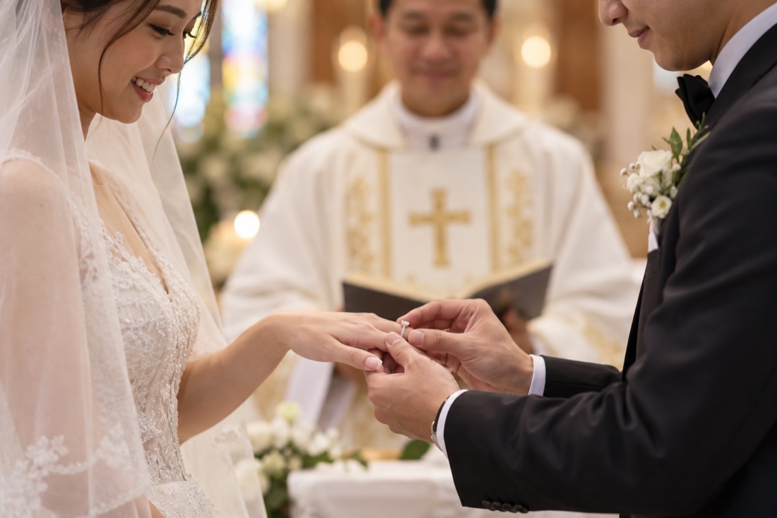 Groom placing the wedding ring on his bride's finger as the priest blesses them during a Catholic wedding Mass in Singapore.